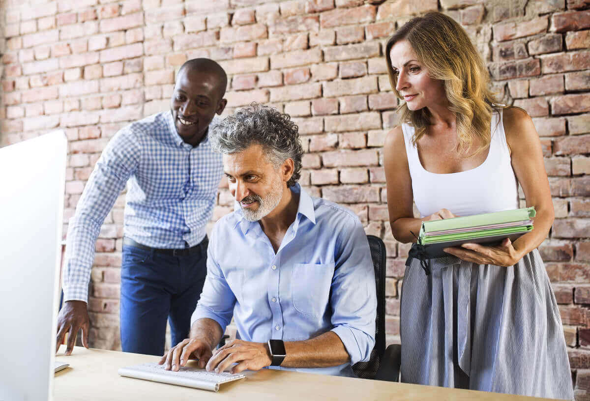 A group of three diverse coworkers gathered around a desktop computer.