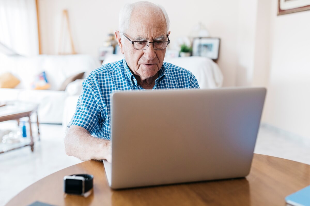 Un homme avec des lunettes est assis à une table et fait une recherche sur son ordinateur portable.