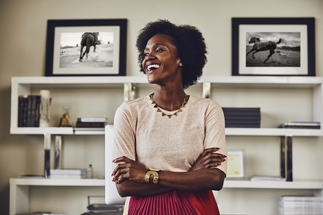 Une femme souriante est dans son bureau, les bras croises.